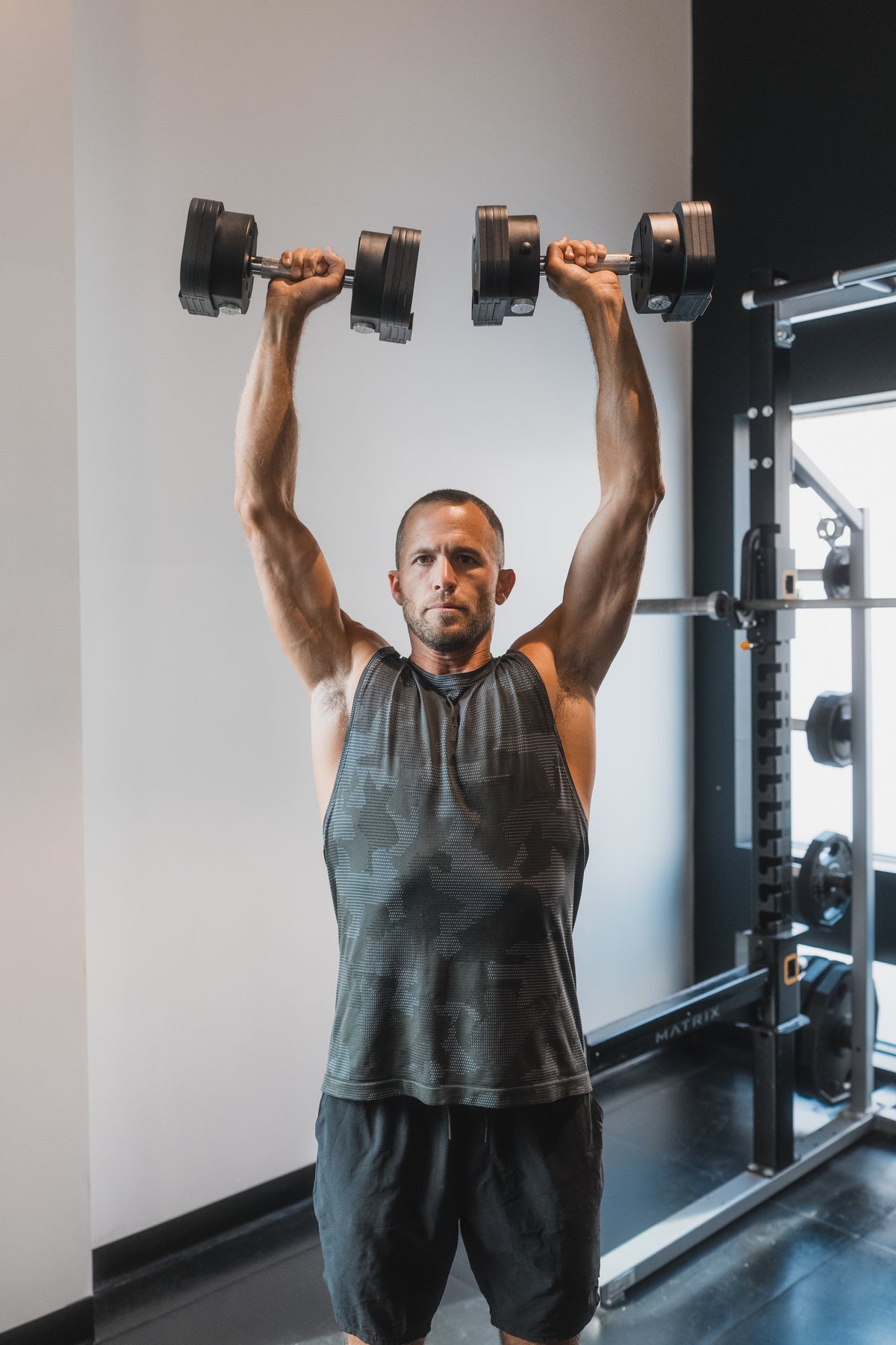 Athlete pressing a pair of MX Select dumbbells overhead in a home gym